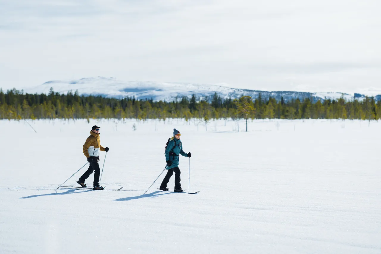 Two cross-country skiers on a frozen lake near Levi, with the fells behind